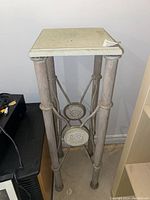 Full view of the metal plant stand showing four cylindrical legs and the square top surface.