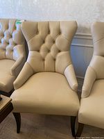 Close-up of beige leather dining chair front showing tufted diamond button back and seat cushioning