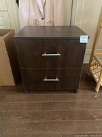 Front view of dark wood nightstand with two drawers and metal pull handles, showing overall condition and style.