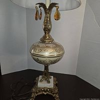 Full view of the vintage embossed bronze/brass table lamp with hand-painted glass and amber glass pendants, cream lampshade, and marble base.