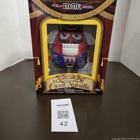 Front view of the M&M Nutcracker candy dispenser in original box, showing red M&M character in nutcracker outfit through window.