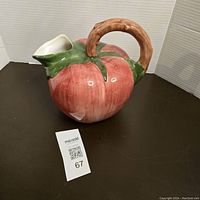 Front view of the ceramic tomato pitcher with curved stem handle, showing major body and spout shape.