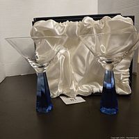 Two clear martini glasses with blue octagon shaped multi-faceted stems, in front of original box with satin lining.