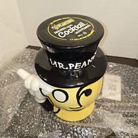 Front and side view of Mr. Peanut ceramic cookie jar with top hat lid showing Planters branding and character details.