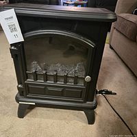 Front view of small black electric fireplace heater with closed glass front door and decorative details.