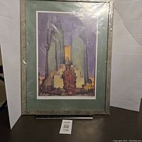Framed art print showing stylized depiction of Flat Iron Building with urban background, measuring approximately 26x20 inches, under glass with some reflections.