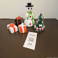 Lot of four vintage glass figurines including snowman, Christmas tree with gifts, and three wrapped gift boxes on black surface with neutral background.