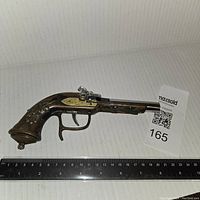 Vintage gun-shaped lighter with brown handle and brass details, alongside ruler showing length approx. 8 inches