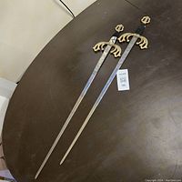 Pair of full-length vintage medieval-style stainless steel swords laid flat on a dark surface, showing blade length and style.