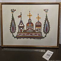 Full view of the framed needlepoint embroidery wall art showing stylized colorful architectural motif with flowers and birds.