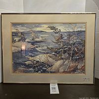Framed landscape print showing a winter lakeside with snow, trees, and rocks. Signed by artist in lower right corner.
