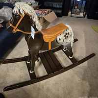 Photo of the vintage wooden rocking horse showing the left side, detailing the body, saddle, and yarn mane and tail.