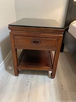 Front view of one bedside table showing drawer, lower shelf, and glass top