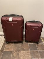 Front view of both Swiss Gear hard shell roller suitcases, maroon color with visible scuff marks on large suitcase.
