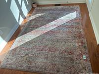 Top view of pink and grey thin area rug with foam underlay on wooden floor, showing pattern and color under natural light.