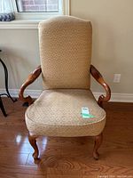 Front view of wood framed arm chair with upholstered beige fabric and tall backrest.