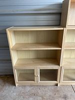 Front view of light wood IKEA bookcase with two open shelves and lower glass paneled doors showing condition and style.