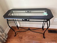 Console table shown from a top and angled view with visible octagonal wood border and glass top, black metal curved legs and stretcher