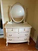 Front view of white painted dresser with oval mirror, showing drawer fronts and mirror frame details.