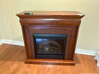 Dimplex electric fireplace with wooden mantle in brown finish, showing front and side angles with remote control on top.