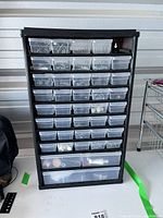 Front view of black plastic hardware organizer with clear drawers filled with various small hardware items.