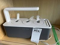 Photo of a Click and Grow herb garden unit with integrated LED grow light, three planting pods, and attached power cord, placed on wooden shelf.