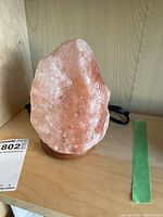 Front view of the Himalayan salt lamp showing natural salt crystal texture and coloration with attached power cord and wooden base.
