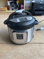 Full front view of the Instant Pot showing control panel and stainless steel body, placed on a floor.