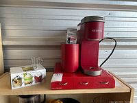 Red Keurig coffee maker with red drawer and boxed glass cups on shelf
