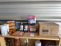 Photo of assorted light bulbs and battery packs on shelf, including a large box of Edison vintage style bulbs and smaller packs of LIFX and Sunbeam bulbs, plus battery packs.