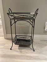 Front view of black metal occasional table showing two shelves and decorative frame.
