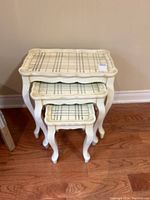 Three white nesting tables stacked, showing striped top surface and curved legs.