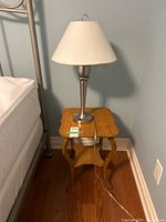 Front side view of small wood night stand with metal table lamp featuring fabric shade on top.