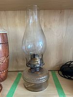 Full view of the vintage glass oil lantern showing the tall clear chimney and the glass base.