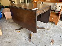 Side view of the pedestal table with one drop leaf extended, showing claw feet on pedestal base and the side drawer.