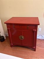 Front view of the red lacquered Asian style cabinet showing two drawers and bottom double doors with brass hardware.