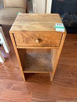 Front view of a small wood table with one drawer and open shelf below, showing the worn finish and aged wear.
