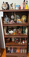 Full view of cabinet showing three main shelves and top surface filled with various items including figurines, lamp, ceramics, and books.