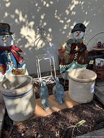 Photo showing large stoneware crocks marked 5 and 6, two metal snowman decorations, and blue ceramic garden statues shaped like birds.