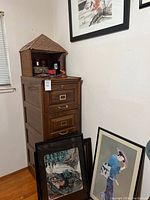 Front view of filing cabinet with miniature house on top, artwork leaning against wall