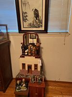 Wide view of lot showing wooden bench with floral cushion, miniature house, cabinet, various Asian figurines arranged atop and in front of furniture.