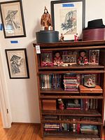 Full view of library cabinet showing framed art on adjacent wall and items arranged on shelves including dolls, books and decor