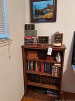 Tall wooden bookshelf with multiple shelves containing books and various decorative items on top, located in corner of room.