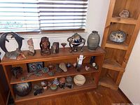 Wide photo showing wood corner shelf unit with two main shelves and various pottery, stone, and wood decor items on shelves and top.