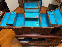 Open rectangular carved wooden jewelry box showing blue velvet interior compartments and mirror.