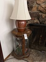 Photo of the wooden side table with curved glass display and ceramic lamp on top by fireplace.