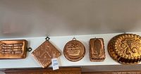 Decorative wall molds hung on a wall: rectangular loaf, diamond, round fruit basket, corn cob, large round fruit motif