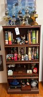 Full view of wooden library cabinet filled with vintage oil lamps, cookbooks, and various collectibles including figurines and pottery.