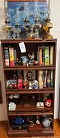 Full view of cabinet with oil lamps on top and shelves filled with books and collectibles