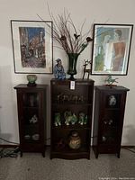 Three display cabinets flanked by two framed art prints with assorted items displayed
